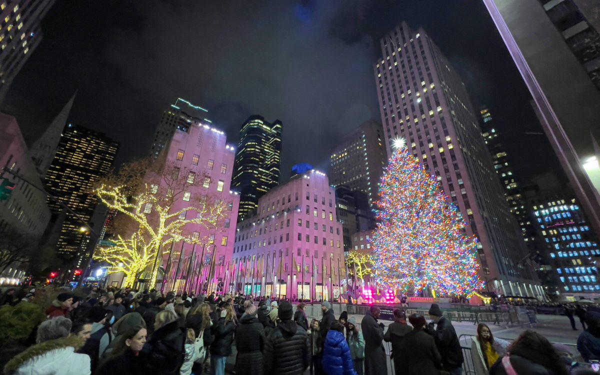 Tourists walk near the illuminated Christmas tree in Rockefeller Center in New York City, on December 8, 2021. (Photo by Daniel SLIM / AFP)