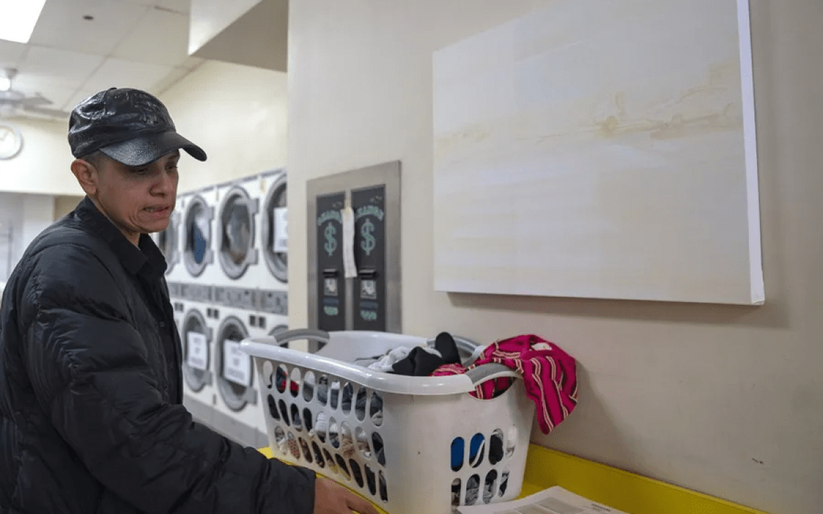 La encargada del proyecto artístico Desnivel, María de Victoria, lava su ropa frente a una obra colgada de la artista Gloria Maximo en una lavandería, en Nueva York (Estados Unidos). EFE/ Ángel Colmenares